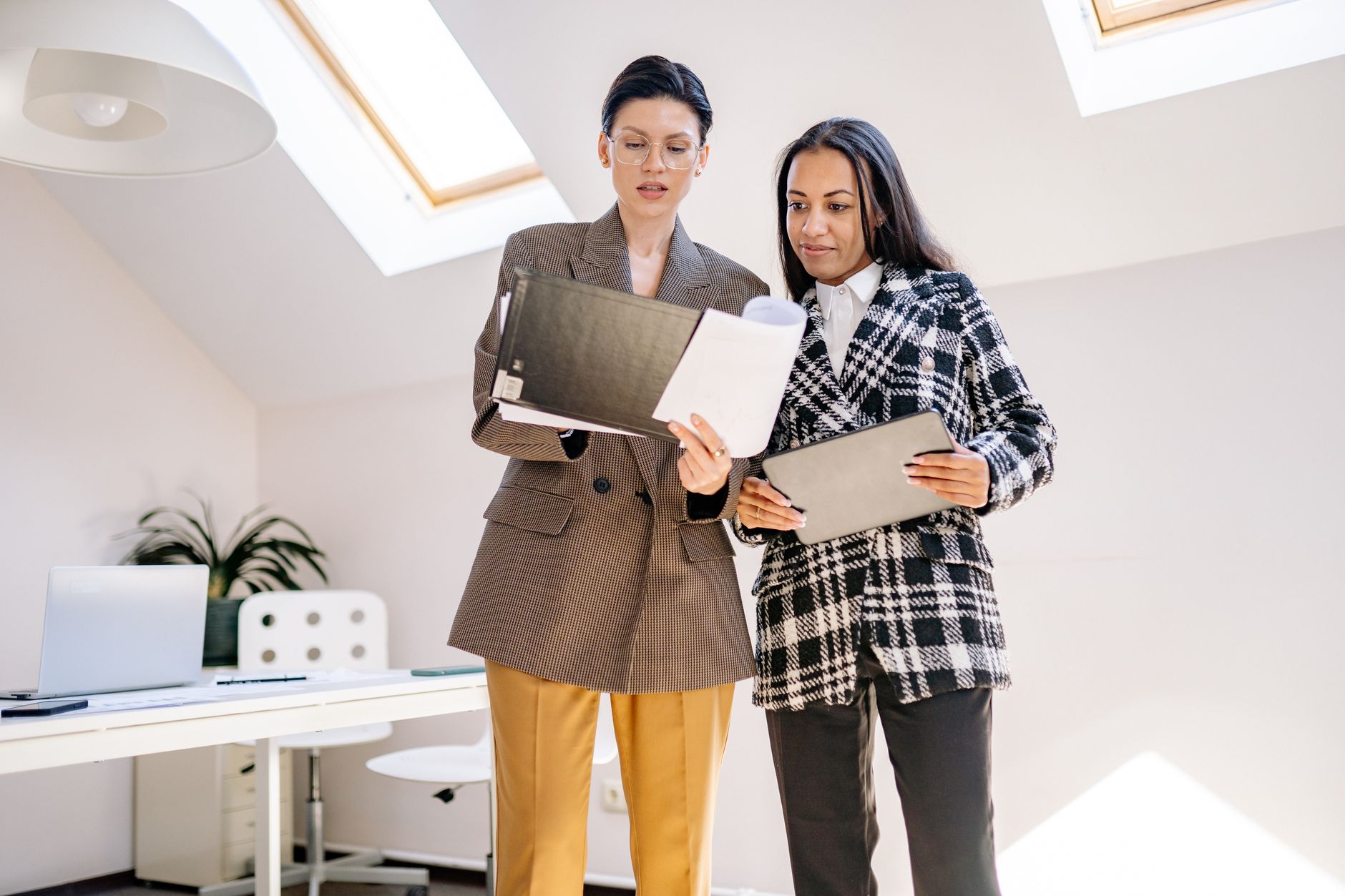 Two colleagues standing in an office, reading and discussing documents together.